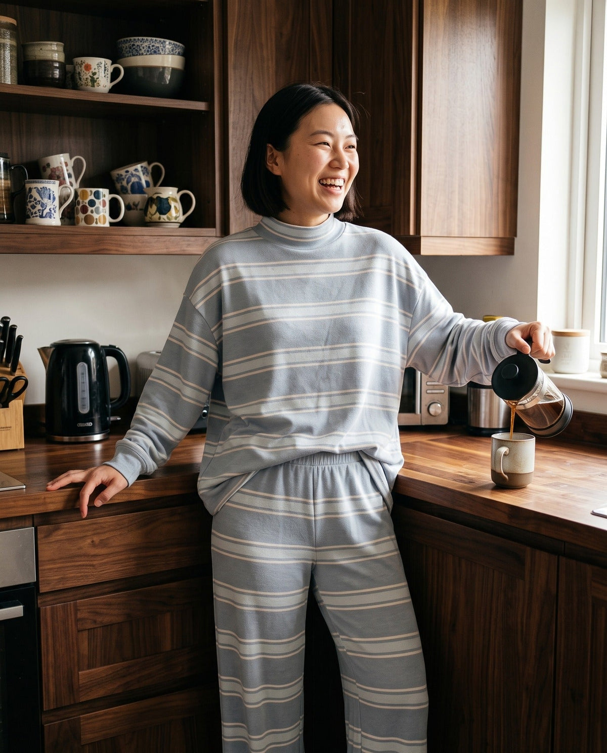 A woman pouring coffee in her kitchen in The Sunday striped lounge set in Light Blue