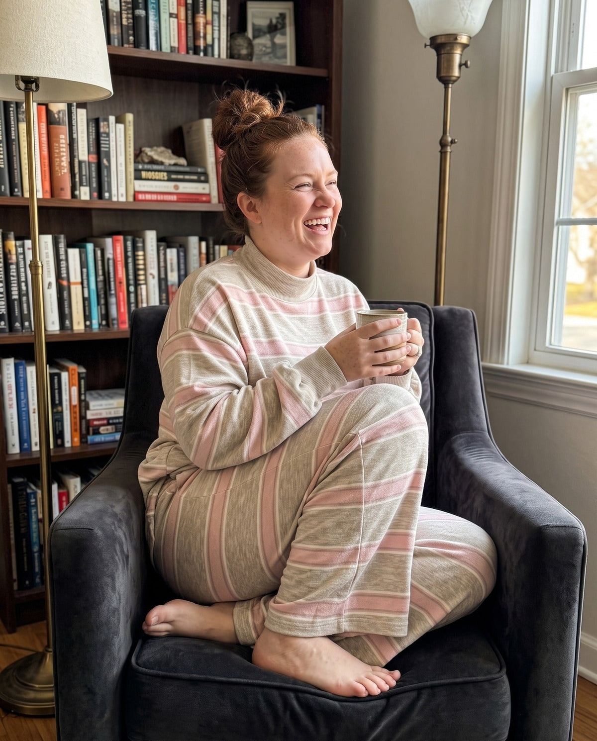 A woman curled in an armchair with a mug in The Sunday striped lounge set in Pink