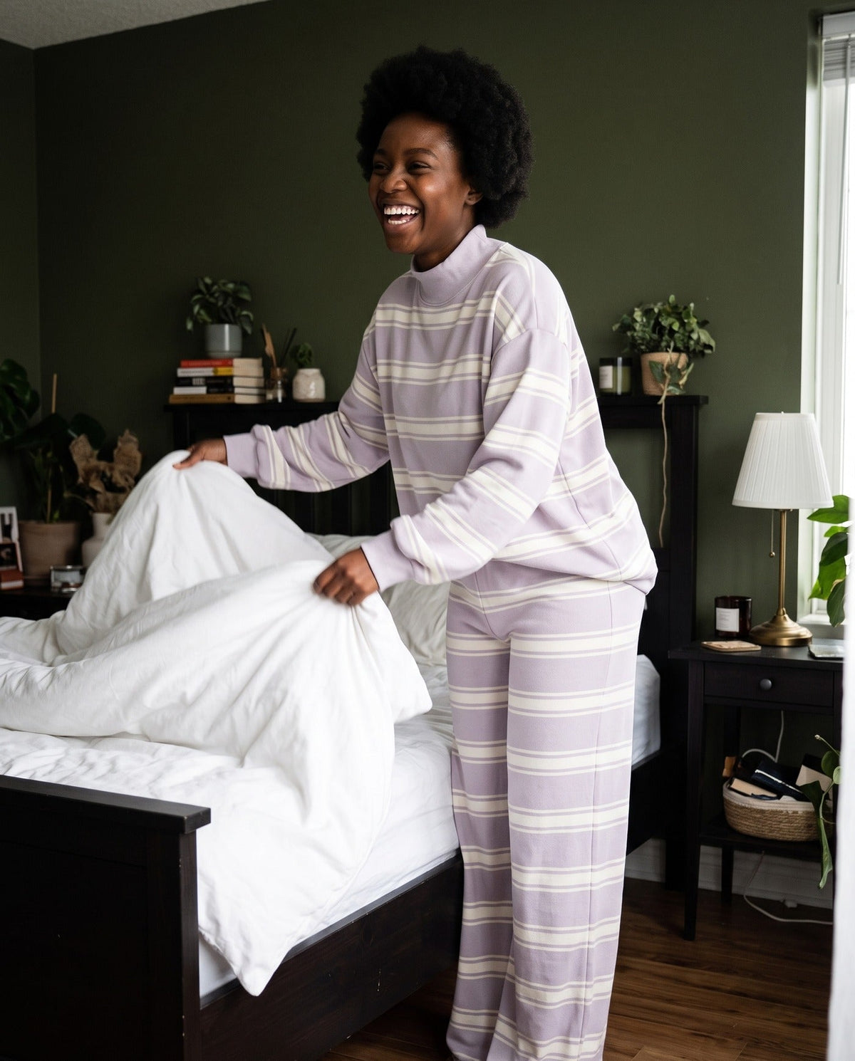 A woman making her bed on a slow morning in The Sunday striped lounge set in Light Purple