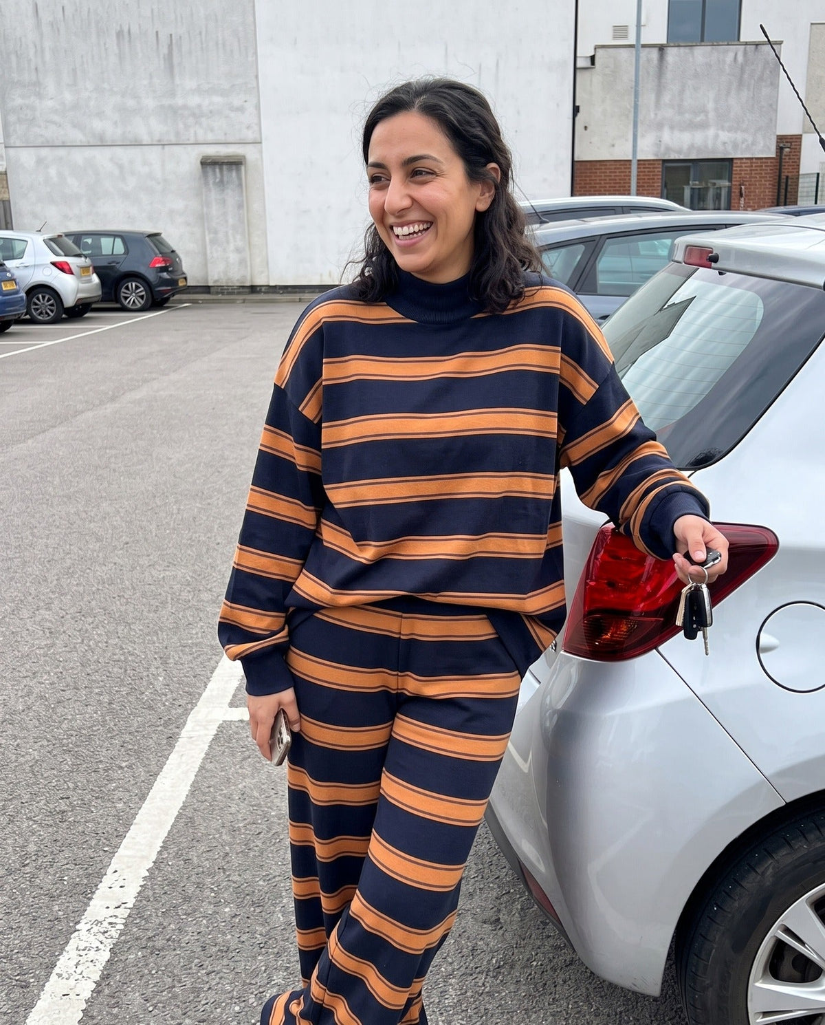 A woman leaning against her car at school pickup in The Sunday striped lounge set in Orange
