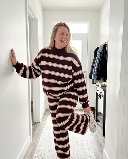 A woman pulling on a sneaker in her hallway in The Sunday striped lounge set in Wine Red