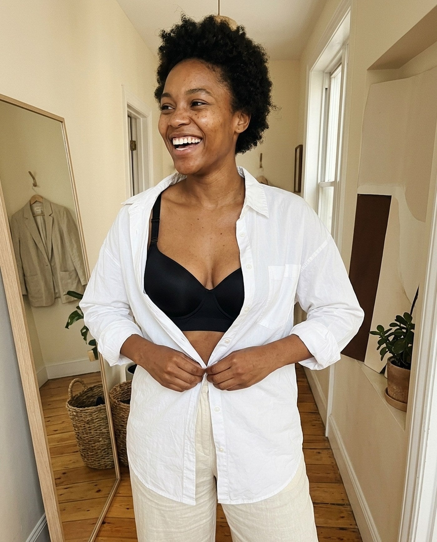 A woman laughing while buttoning a shirt over The Ease wireless smoothing bra in Black